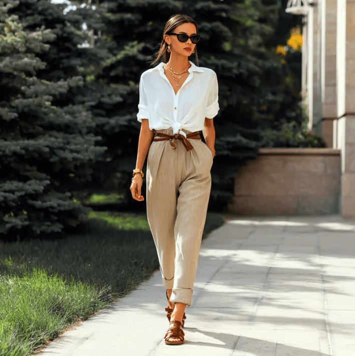 Fashionable woman in a white shirt and beige pants walking outdoors, exuding style and confidence.