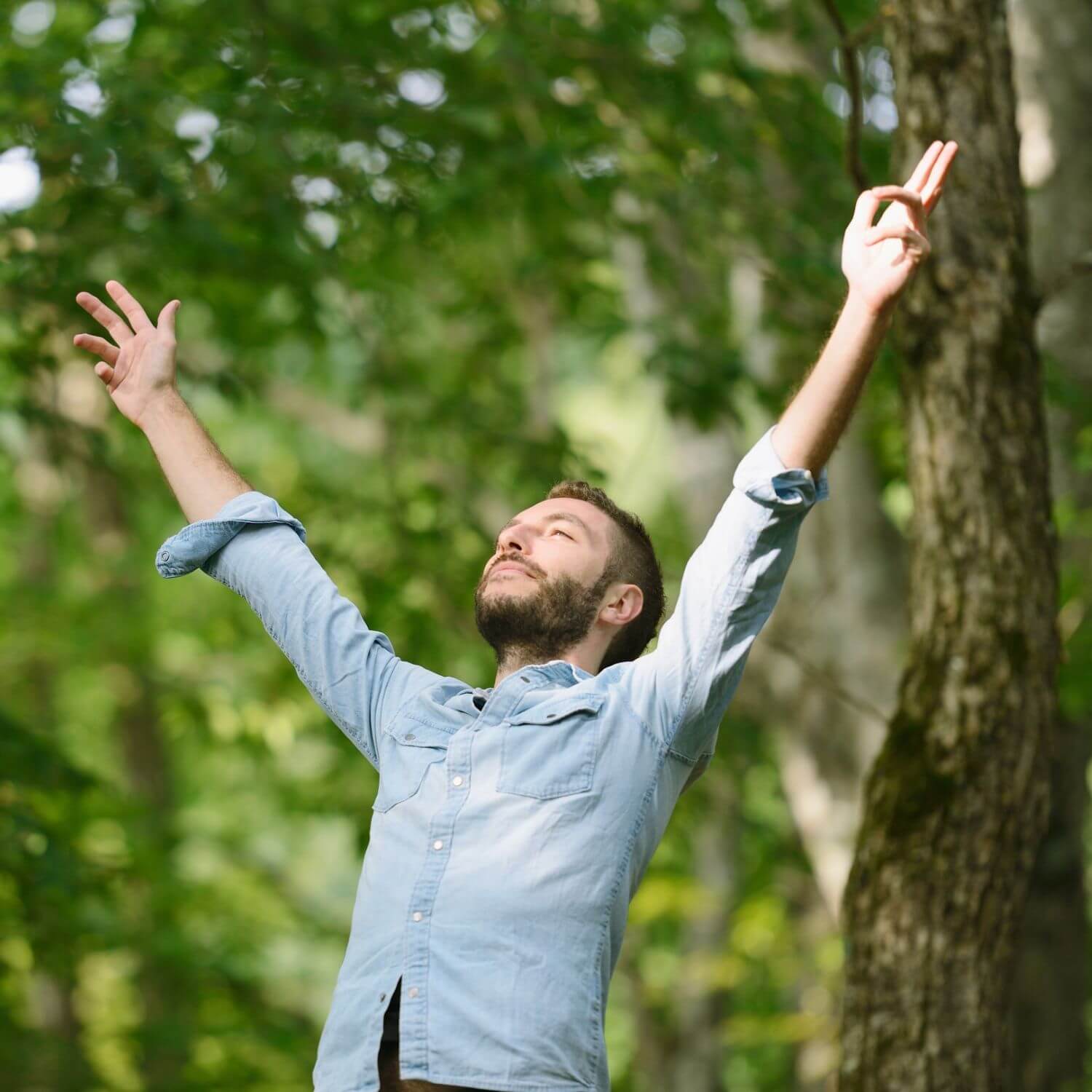 Man outdoors with arms raised, enjoying nature and feeling refreshed in a vibrant green forest.