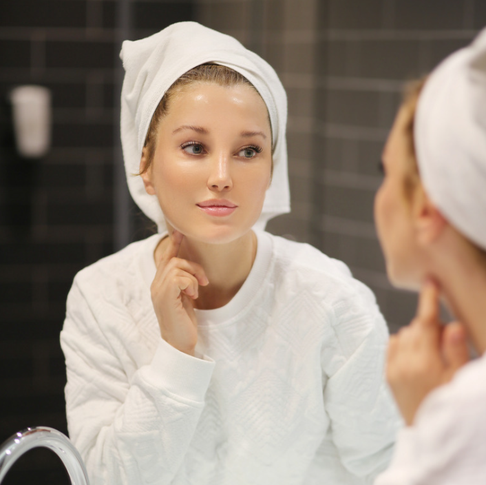 A woman applying Pure Refreshing Serum in a bathroom mirror, showcasing a smooth skincare routine.
