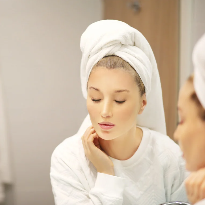 Woman applying Fresh Repair Cream in a bathroom, wrapped in a towel, focusing on skincare routine.