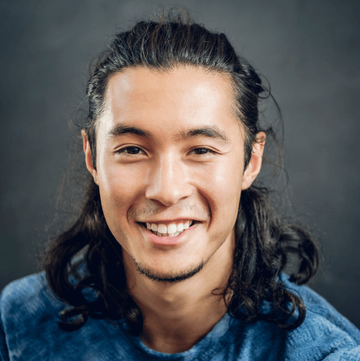 Smiling man with long hair wearing a blue shirt, representing confidence and wellness for promoting Vital Support Gel.