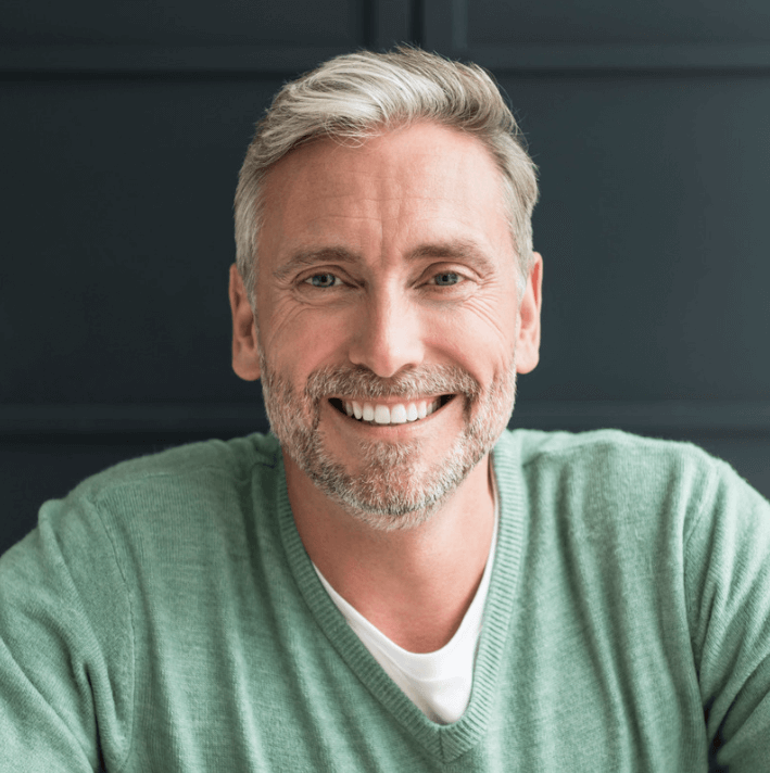 Smiling middle-aged man wearing a green sweater, showcasing a friendly and approachable demeanor.