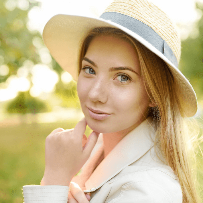 A young woman in a straw hat enjoys a sunny day outdoors, showcasing her natural beauty and relaxed demeanor.