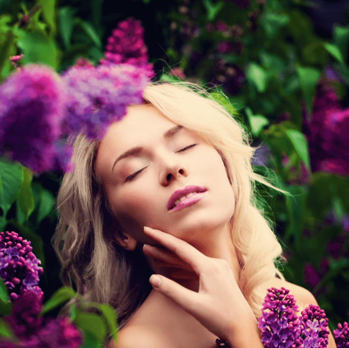Woman enjoying natural beauty amidst blooming lilacs, representing the refreshing effect of Multi Care Essence.