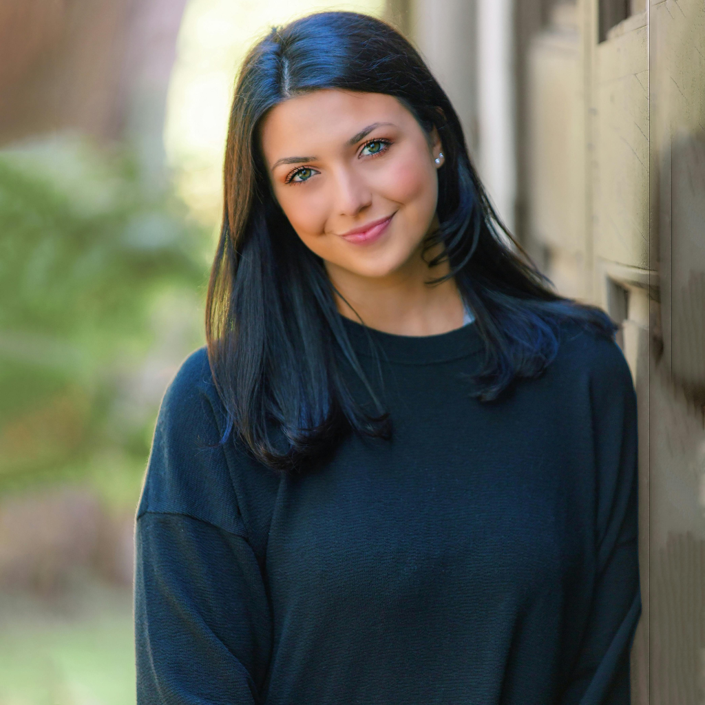 Smiling woman in a black sweater with shiny, smooth hair showcasing the effects of Batana Oil & Rosemary Shampoo.
