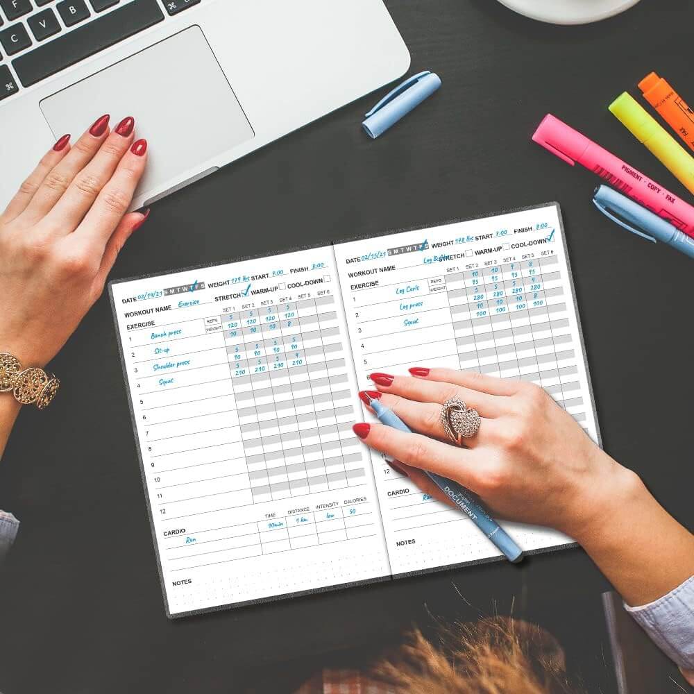Zentheca Planner Journal open on a table with hands writing, showcasing fitness tracking for workouts.
